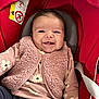 baby, smiling, infant, car_seat, pink_vest, floral_pattern, clothing, happy, cute, child, seatbelt, red, portrait, indoors, person, young_child, face, apparel, sitting, cozy