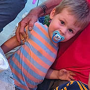 Jasiah joined the competition — help win amazing prizes! child, toddler, pacifier, striped_shirt, orange, gray, adult_hand, red_shirt, curious, outdoor, evening_light, portrait, person, casual_clothing, holding_hand, closeup, face, young_child, cute, gentle
