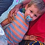 child, toddler, pacifier, striped_shirt, orange, gray, adult_hand, red_shirt, curious, outdoor, evening_light, portrait, person, casual_clothing, holding_hand, closeup, face, young_child, cute, gentle