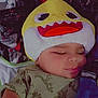 baby, blanket, child, clothing, cozy, cute, dinosaur_print, face, hat, headwear, indoor, infant, nap, person, resting, shark_hat, sleeping, soft_lighting, toddler, yellow