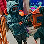 child, hoodie, toy_gun, goggles, indoor, carpet, fish_tank, wooden_chair, curtains, person, furniture, mask, shoes, sleeves, window, floor, room, play, kid, casual