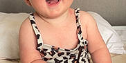 Naveah is registered to the contest to win money with this photo: baby, infant, child, smiling, happy, sitting, bed, bedding, leopard_print, clothing, person, face, hand, foot, head, eyewear, sunglasses, indoor, cute, expression