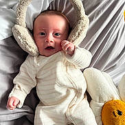 Clara joined the competition — help win amazing prizes! baby, infant, earmuffs, plush_toy, daisy, bed, blanket, sleepwear, soft_texture, cute, child, smile, face, hand, lying_down, cozy, indoor, comfort, toy, expression
