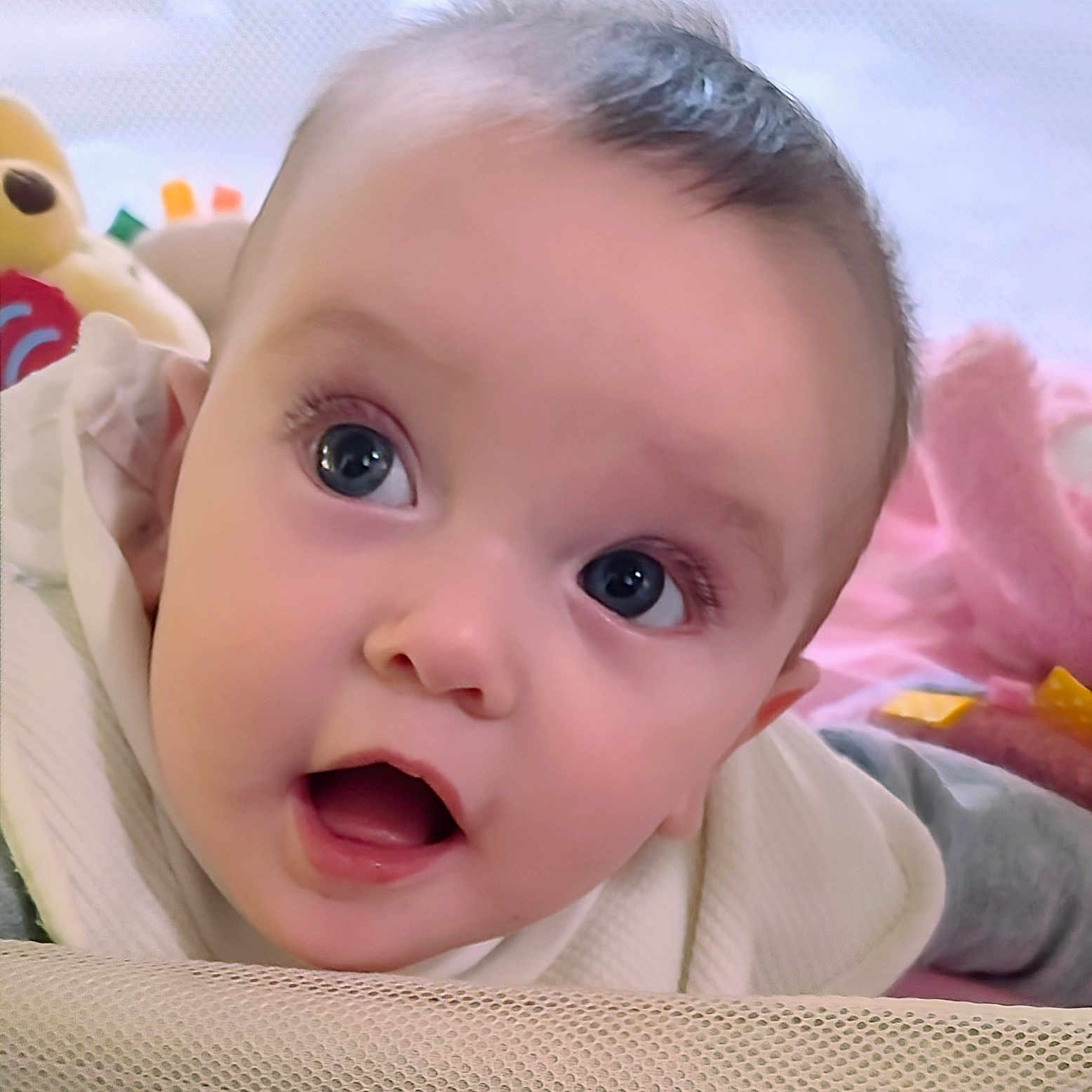 Marian is registered to the contest to win money with this photo: baby, blanket, child, closeup, curious, cute, expression, eyes, face, head, indoors, infant, mouth, pink, playpen, portrait, skin, soft_toys, white_clothing, young