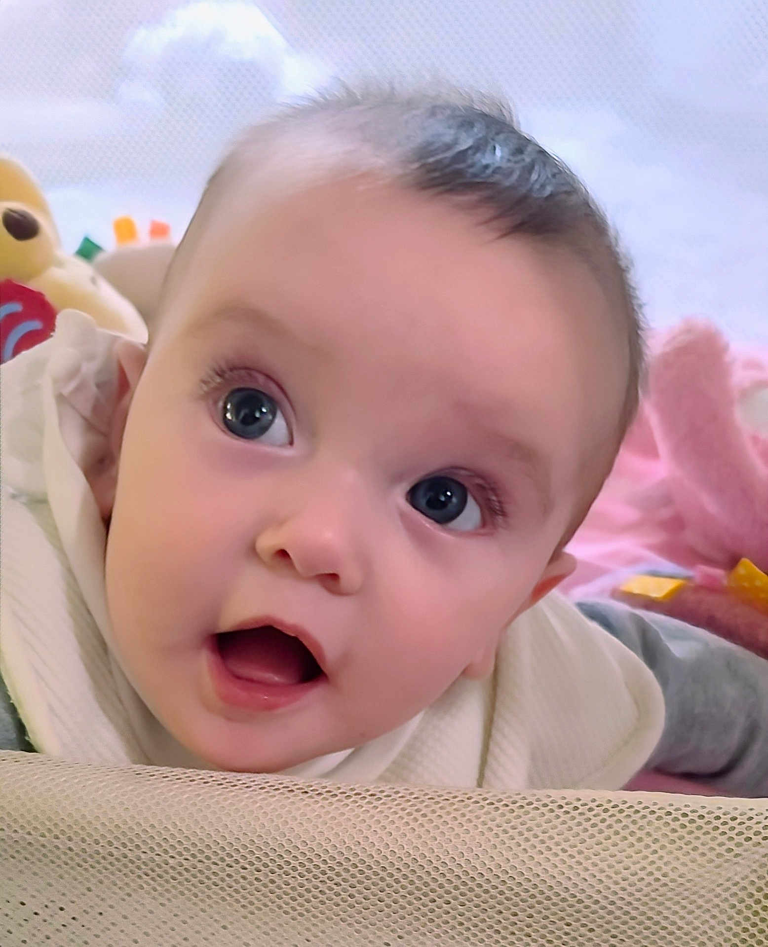 Marian is registered to the contest to win money with this photo: baby, infant, face, eyes, mouth, curious, playpen, blanket, soft_toys, pink, white_clothing, closeup, child, cute, indoors, portrait, skin, head, expression, young