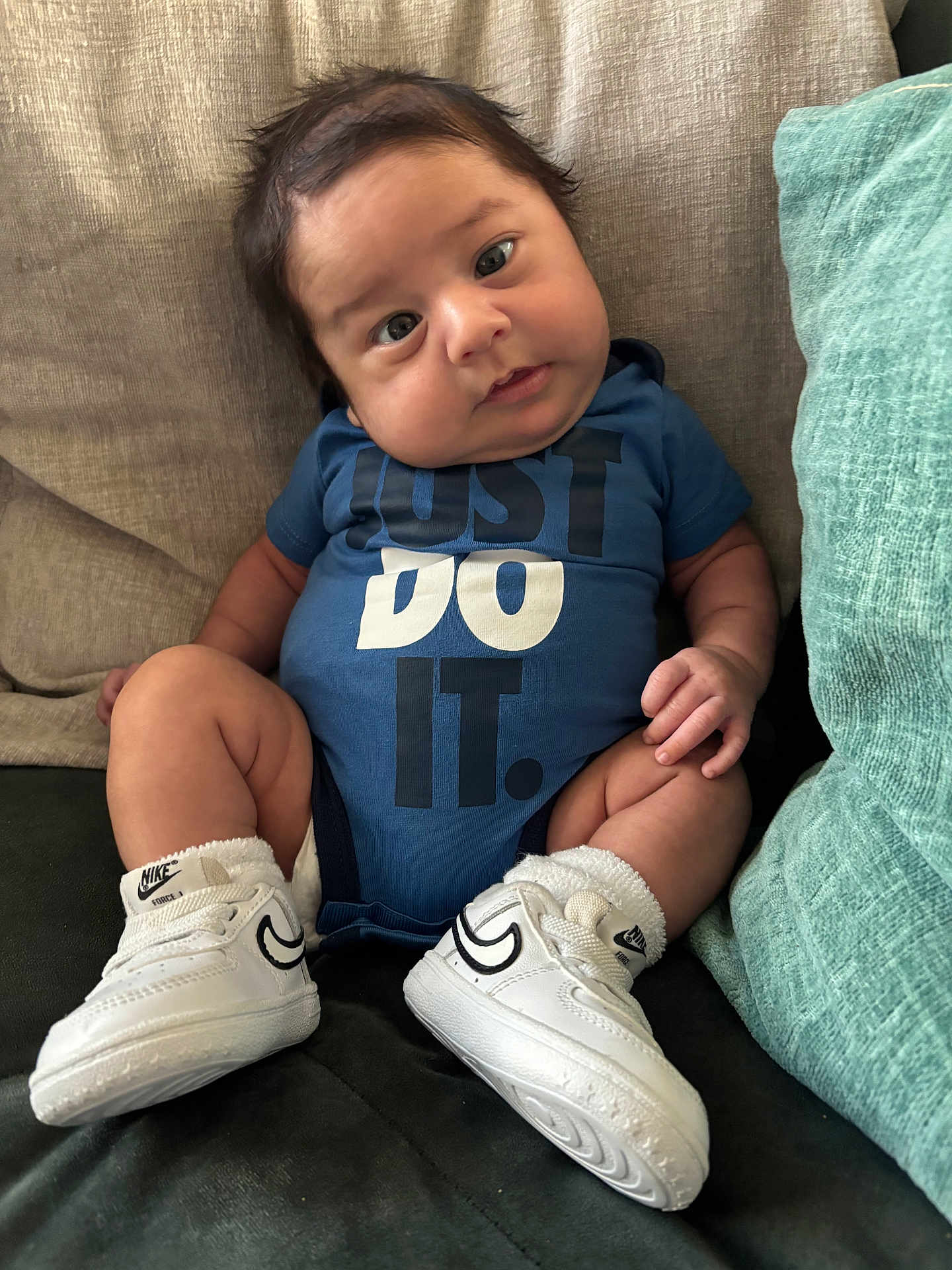 Ryder is registered to the contest to win money with this photo: baby, infant, blue_onesie, nike_shoes, sneakers, couch, cushion, cute, child, indoor, portrait, sitting, clothing, footwear, head_tilt, expression, soft_fabric, young_child, casual, comfortable