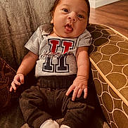Ryder is registered to the contest to win money with this photo: baby, infant, child, cute, face, tongue_out, clothing, shirt, pants, socks, chair, furniture, home, comfortable, seated, expression, skin, hands, feet, indoors