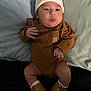 Ryder is registered to the contest to win money with this photo: baby, infant, beanie, brown_onesie, boots, bed, pillow, cute, chubby_cheeks, clothing, portrait, child, indoors, expression, small_hands, footwear, laying_down, soft_lighting, casual, adorable