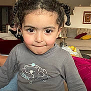 Mélina a rejoint le concours — aidez-le/la à gagner de superbes lots ! child, pigtails, braided_hair, gray_shirt, bear_illustration, indoor, living_room, cushions, table, snacks, sofa, playful_expression, brown_eyes, curly_hair, cozy, person, portrait, smirk, casual_clothing, home