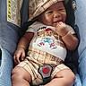 baby, infant, car_seat, plaid_hat, plaid_shorts, white_onesie, socks, smiling, cute, child, seat_belt, indoor, comfort, happy, face, hand, footwear, clothing, baby_accessory, portrait
