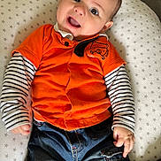 Hakan a rejoint le concours — aidez-le/la à gagner de superbes lots ! baby, child, smiling, orange_shirt, striped_sleeves, blue_jeans, cushion, star_pattern, face, happy, indoors, seated, clothing, person, cute, young_child, portrait, jeans, long_sleeve, comfort
