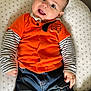 baby, child, smiling, orange_shirt, striped_sleeves, blue_jeans, cushion, star_pattern, face, happy, indoors, seated, clothing, person, cute, young_child, portrait, jeans, long_sleeve, comfort