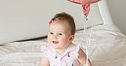 Kristina joined the competition — help win amazing prizes! baby, child, balloon, pink_balloon, bed, blanket, dress, sailboat_pattern, hair_clip, smiling, sitting, indoors, cute, infant, ribbons, happy, portrait, soft_lighting, cozy, young_child