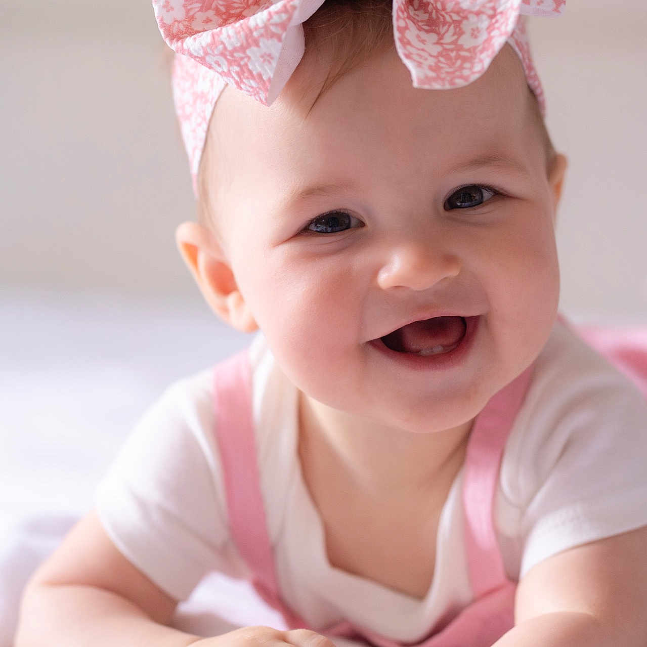 Kristina is registered to the contest to win money with this photo: baby, child, smiling, headband, bow, pink, white_clothing, infant, portrait, close_up, happy, cute, face, skin, hands, lying_down, indoors, soft_light, young, person