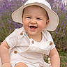 Kristina joined the competition — help win amazing prizes! baby, child, smiling, hat, white_clothing, overalls, grass, outdoor, nature, flower, purple_flower, happy, cute, infant, portrait, sun_hat, daylight, sitting, greenery, blurred_background