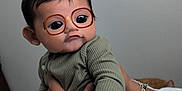 Nicolas is registered to the contest to win money with this photo: adult_hand, baby, bracelet, cartoon_eyes, child, cute, expression, face_filter, glasses, green_clothing, hand, hello_kitty, holding, indoor, person, playful, portrait, shirt, skin, wall