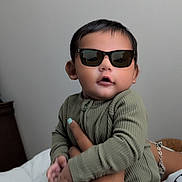 Nicolas joined the competition — help win amazing prizes! accessory, baby, bed, bracelet, child, cool, cute, fashion, green_outfit, hand, holding, indoor, infant, neutral_background, person, portrait, sitting, sunglasses, white_bedspread, young_child