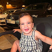 Ilia is registered to the contest to win money with this photo: toddler, child, smile, happy, chair, outdoor, night, urban, car, parking, romper, person, face, cute, baby, skin, seat, expression, light, background