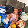 baby, child, plush_toy, couch, pillow, sofa, indoor, soft_toy, stuffed_animal, child_sitting, casual_clothing, white_socks, relaxed, cute, home, colorful, decor, toy, infant, portrait