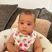 Sonia is registered to the contest to win money with this photo: baby, infant, bib, strawberry_pattern, bottle, baby_seat, teddy_bear_print, couch, pillow, arm, hand, face, eyes, curious, indoor, child, person, clothing, seat, comfort