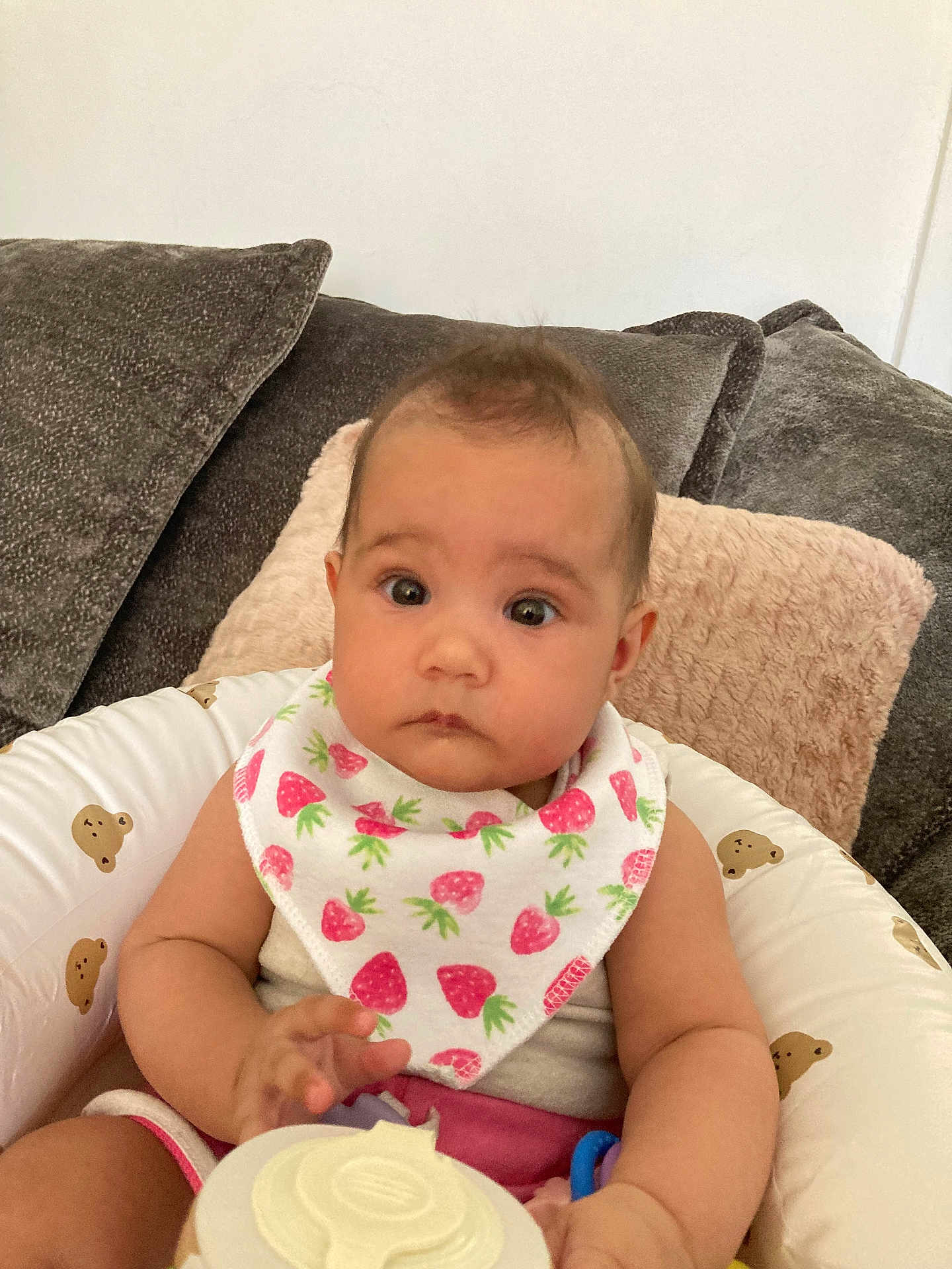 Sonia is registered to the contest to win money with this photo: baby, infant, bib, strawberry_pattern, bottle, baby_seat, teddy_bear_print, couch, pillow, arm, hand, face, eyes, curious, indoor, child, person, clothing, seat, comfort