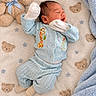 newborn, baby, infant, sleeping, yawning, lying_down, portrait, face, teddy_bear, stuffed_animal, blanket, blue_clothing, mittens, knitwear, nursery, indoor, cozy, soft, bear_pattern, cuddly
