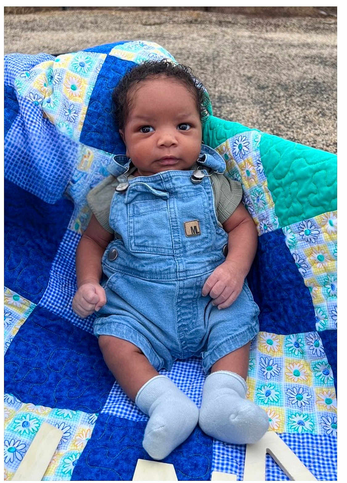 Jo Jo joined the competition — help win amazing prizes! baby, child, denim_overalls, socks, curly_hair, patchwork_quilt, blue, green, yellow, flower_pattern, outdoor, infant, cute, portrait, sitting, hands, feet, clothing, person, young