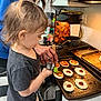 Evie is registered to the contest to win money with this photo: toddler, child, adult, kitchen, cooking, baking_tray, dough, sauce, stove, countertop, utensil, spoon, hair_tie, appliance, cutting_board, food_preparation, person, indoor, helping, family