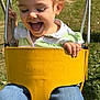 toddler, child, swing, yellow_swing, outdoor, playground, happy, smiling, grass, daylight, jeans, green_shirt, short_hair, holding, fun, sunny, park, metal_chains, casual_clothing, joy