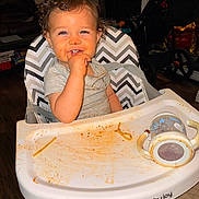 Prynce is registered to the contest to win money with this photo: toddler, child, baby, high_chair, smiling, curly_hair, brown_hair, indoor, portrait, sitting, eating, snack, food, sippy_cup, tray, stroller, home, furniture, happy, face