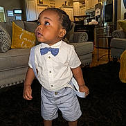 Khyren is registered to the contest to win money with this photo: child, toddler, boy, portrait, standing, formal_wear, bow_tie, suspenders, shirt, shorts, socks, curly_hair, expression, indoors, living_room, kitchen, sofa, cushions, rug, home