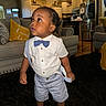 child, toddler, boy, portrait, standing, formal_wear, bow_tie, suspenders, shirt, shorts, socks, curly_hair, expression, indoors, living_room, kitchen, sofa, cushions, rug, home