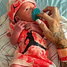 newborn, baby, infant, hospital, hospital_bed, pacifier, red_outfit, hat, cap, blanket, bedding, hand, tattoo, adult, caregiver, portrait, lying_down, indoor, medical_wristband, family