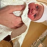 newborn, baby, infant, child, face, eyes, wide_eyed, blanket, swaddled, hat, textile, hand, adult_hand, portrait, indoors, hospital, nursery, close_up, candid, family