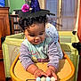 toddler, child, baby, high_chair, toy, beads, witch_hat, curly_hair, indoor, wooden_furniture, playful, cute, purple_clothing, smiling, face, hands, window, curtains, bookshelf, decor