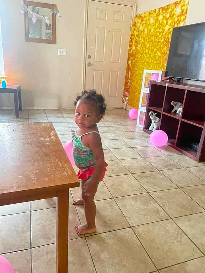 Iyanah is registered to the contest to win money with this photo: beauty, cabinetry, chest_of_drawers, child, door, drawer, dress, floor, flooring, furniture, hardwood, kitchen, material_property, person, picture_frame, pink, shorts, table, television, toddler