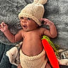 Kartier is registered to the contest to win money with this photo: baby, infant, knitted_hat, knitted_diaper_cover, carrot_toy, soft_blanket, lying_down, surprised_expression, cute, child, hand, face, headwear, plush_toy, cozy, newborn, skin, indoors, portrait, baby_clothing