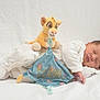 baby, newborn, sleeping, plush_toy, simba, soft_toy, white_clothing, blanket, blue_cloth, name_tag, cute, peaceful, infant, portrait, child, resting, indoors, soft_lighting, cozy, comfortable
