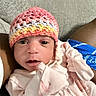 Caylani is registered to the contest to win money with this photo: baby, newborn, infant, knitted_hat, pink_clothing, couch, texture, closeup, portrait, indoors, person, cute, small_hands, wide_eyes, cozy, soft_lighting, fabric, relaxed, resting, casual