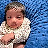 baby, infant, child, floral_clothing, onesie, blue_cushion, plush, soft_texture, indoors, portrait, hand, face, curly_hair, newborn, resting, closeup, young, person, cozy, comfort