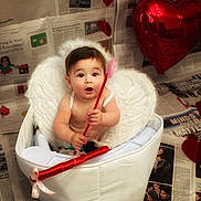 Kreg is registered to the contest to win money with this photo: baby, child, wings, cupid, heart, arrow, basket, newspaper, balloon, red, white, costume, halo, cute, portrait, indoor, celebration, valentines_day, smiling, person