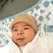 Juan is registered to the contest to win money with this photo: baby, infant, knit_hat, white_jacket, blanket, soft_texture, face, portrait, lying_down, curious_expression, indoors, warm_clothing, child, cute, young, cozy, closeup, zipped_jacket, patterned_blanket, headwear