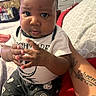 baby, child, infant, person, clothing, hand, face, tattoo, sitting, indoor, bed, pillow, drawer, pattern, curious, cute, expression, black_pants, white_shirt, halloween