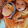 baby, plush_toy, tigger, orange_outfit, bear_ears, blanket, soft_texture, child, cute, wide_eyes, cozy, bed, stuffed_animal, smiling, infant, clothing, indoors, warm_colors, person, portrait