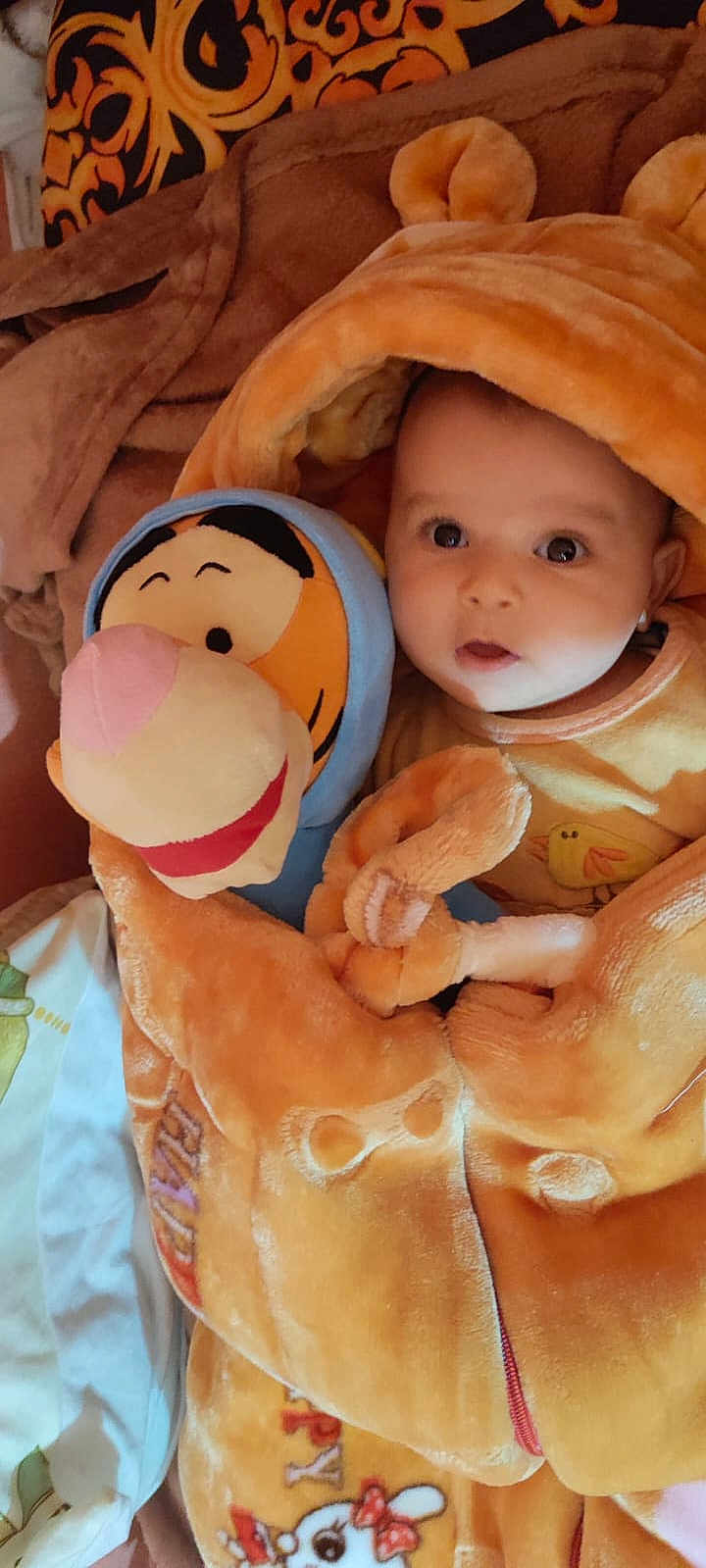 Ryan Hegazi a rejoint le concours — aidez-le/la à gagner de superbes lots ! baby, plush_toy, tigger, orange_outfit, bear_ears, blanket, soft_texture, child, cute, wide_eyes, cozy, bed, stuffed_animal, smiling, infant, clothing, indoors, warm_colors, person, portrait