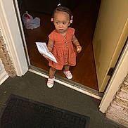 Alina joined the competition — help win amazing prizes! toddler, child, doorway, orange_dress, pink_shoes, hair_beads, paper, snack, indoor, floor, door, threshold, curious, standing, young_child, wood_floor, mat, casual_clothing, home, person