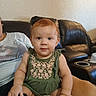 baby, child, infant, portrait, sitting, smiling, red_hair, floral_outfit, green_clothing, earrings, living_room, leather_couch, recliner, indoor, home, adult, lap, family, closeup, photography