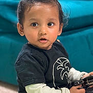 Kian Vidmay Nalabola joined the competition — help win amazing prizes! toddler, child, indoor, toy, black_shirt, long_sleeve, curly_hair, face, eyes, expression, sitting, sofa, blurred_background, hand, casual_clothing, young_child, portrait, candid, person, home