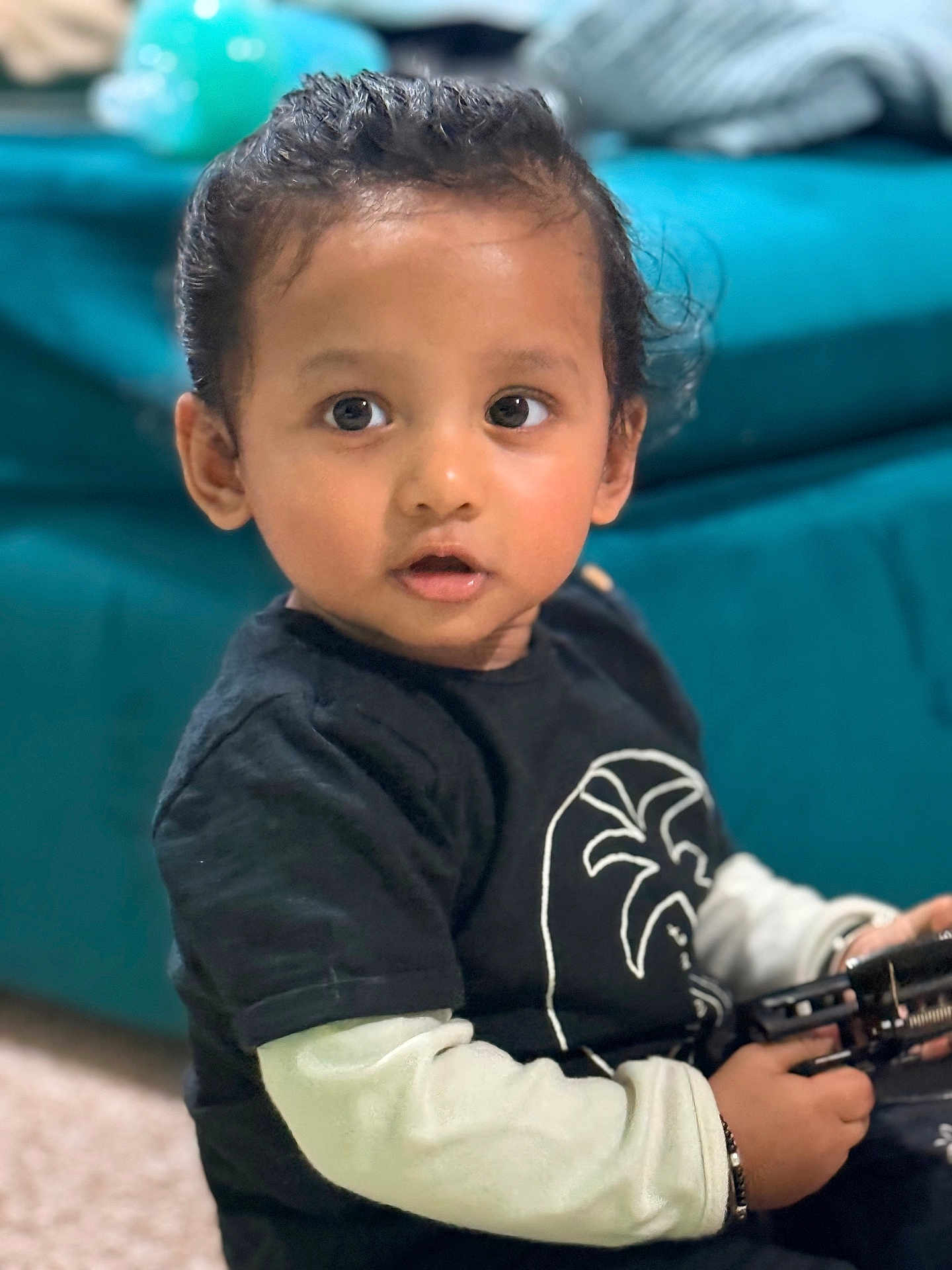 Kian Vidmay Nalabola joined the competition — help win amazing prizes! toddler, child, indoor, toy, black_shirt, long_sleeve, curly_hair, face, eyes, expression, sitting, sofa, blurred_background, hand, casual_clothing, young_child, portrait, candid, person, home