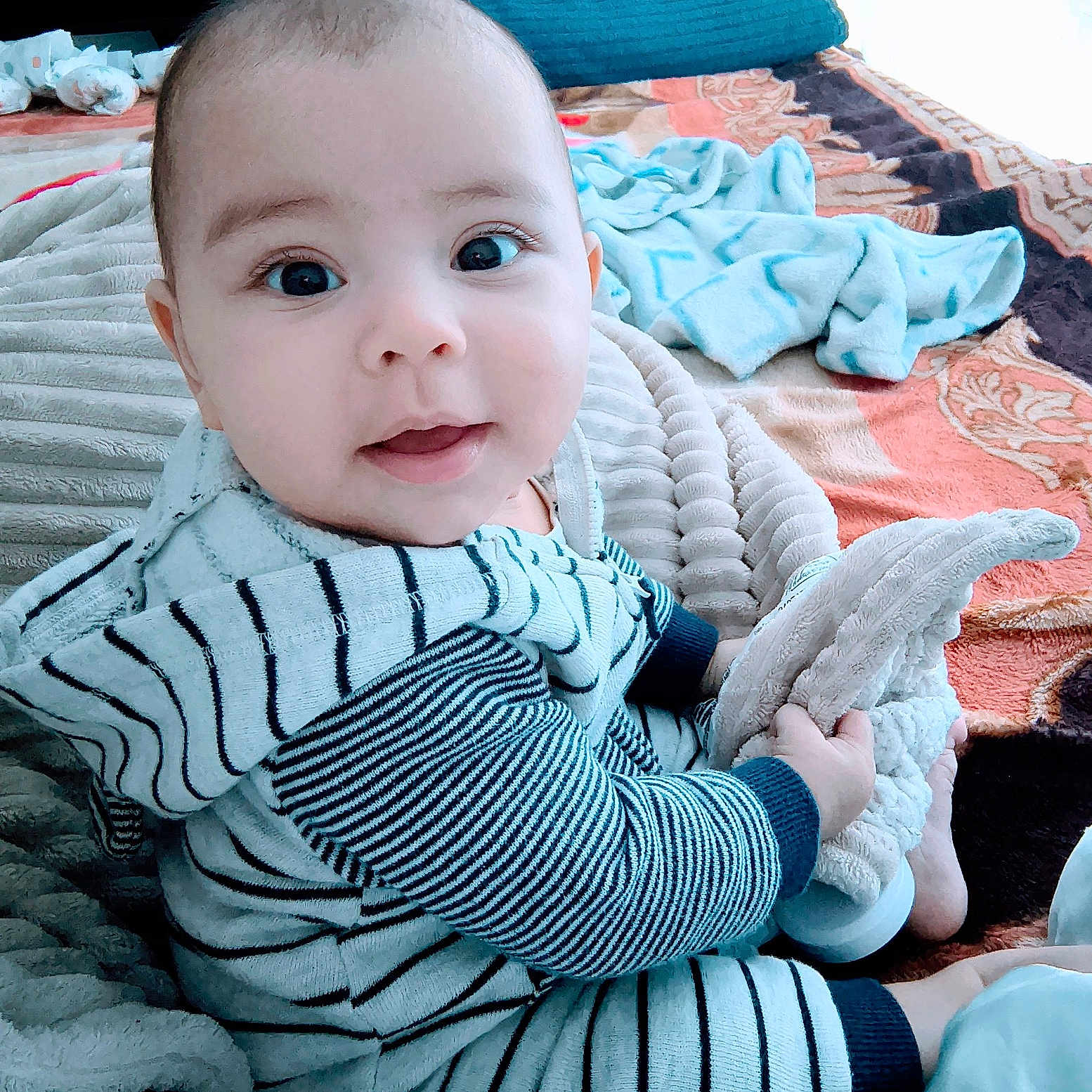 Eliam joined the competition — help win amazing prizes! baby, bed, blanket, child, comfort, cozy, cute, expression, face, happy, indoors, infant, person, plush_toy, sitting, smiling, soft_toy, striped_clothing, warm, young